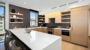 A modern kitchen with a central island, built-in shelves, and a large window.