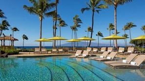 A pool area with lounge chairs and umbrellas, palm trees, and a view of the ocean. - Experience Tropical Bliss at Hyatt Vacation Club at Ka'anapali Beach Resort-2 Bd (Lahaina)