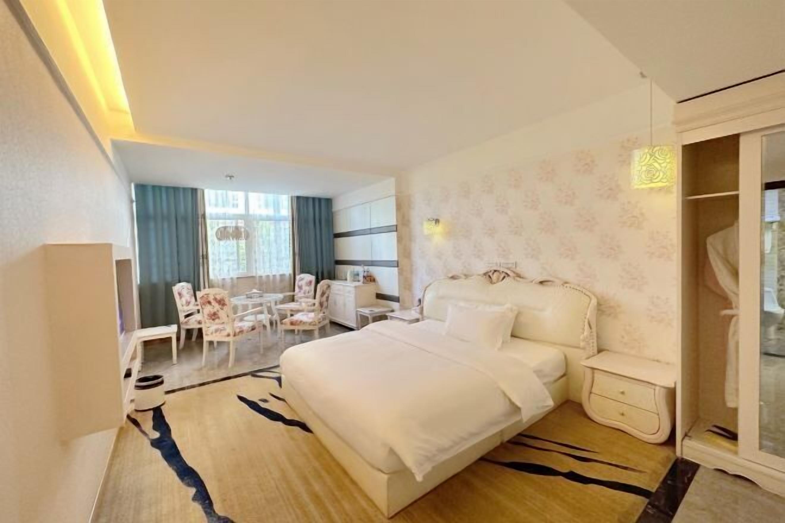 A hotel room with a large bed, a sitting area with chairs, a desk, and a wardrobe.