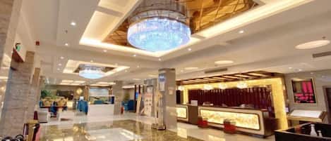A hotel lobby with a reception desk, seating area, and a chandelier.