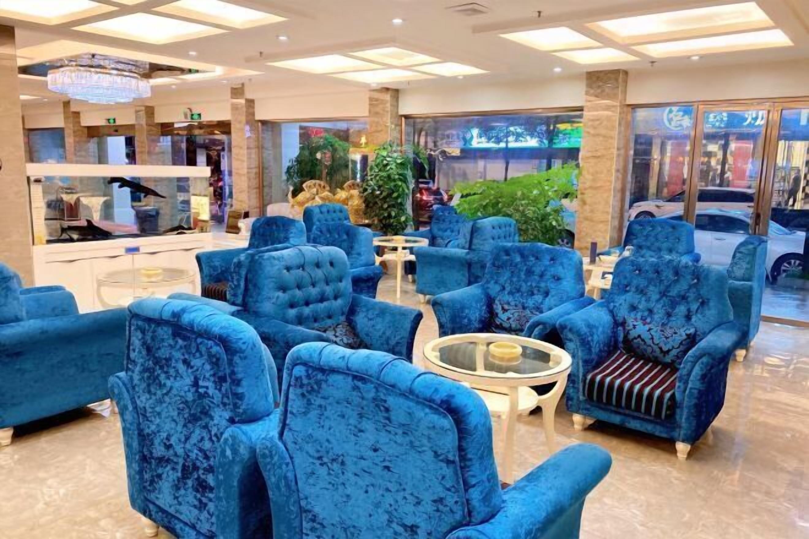 A lobby with blue upholstered chairs, a chandelier, and a glass display case with items.