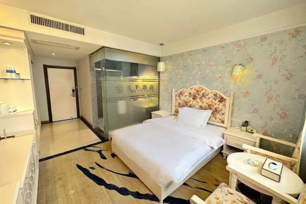 Habitación de hotel con cama, mesita de noche y velador. Se observa una puerta que da a otra habitación y una pared con estampado floral.