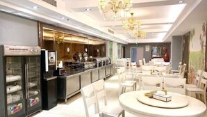 Eine Hotelhalle mit einem Buffetbereich, weißen Stühlen und einer Chandelier.