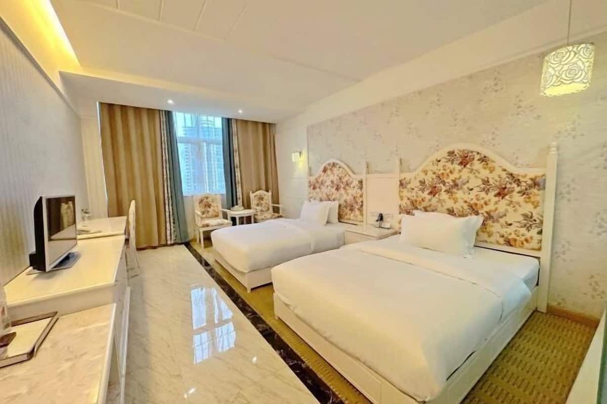 Habitación de hotel con dos camas, un escritorio, una silla y un televisor.