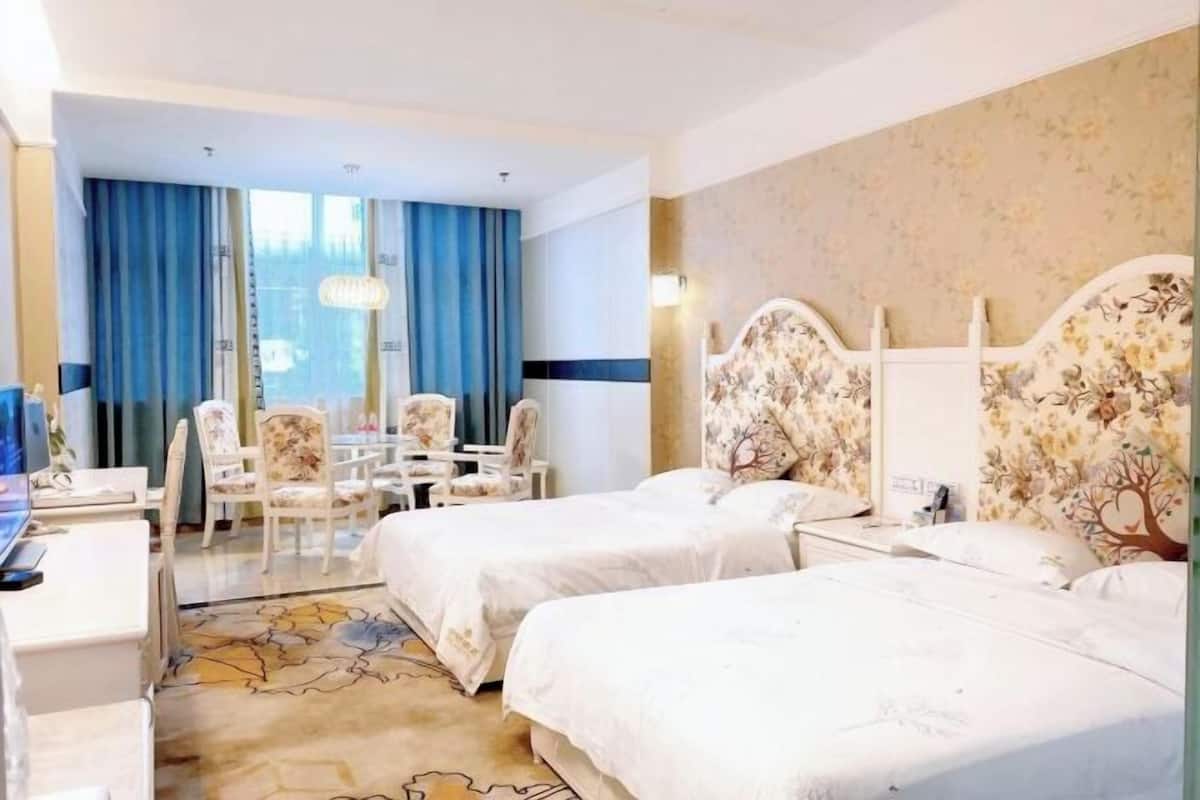 Habitación de hotel con dos camas, un escritorio, una silla y vistas al exterior.