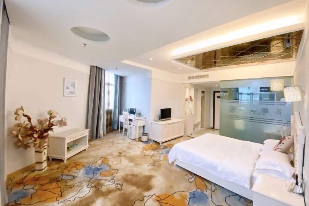 Habitación de hotel con cama, escritorio con computadora, televisor y un jarrón decorativo.