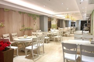 Un comedor amplio con varias mesas redondas y sillas blancas, que presenta una paleta de colores neutros y una decoración moderna.