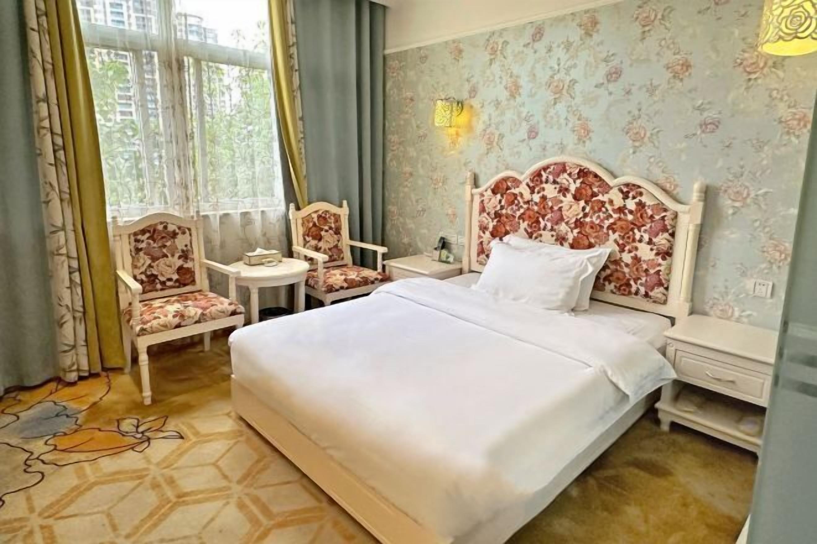 A hotel room with a large bed, two chairs, a small table, and a nightstand.