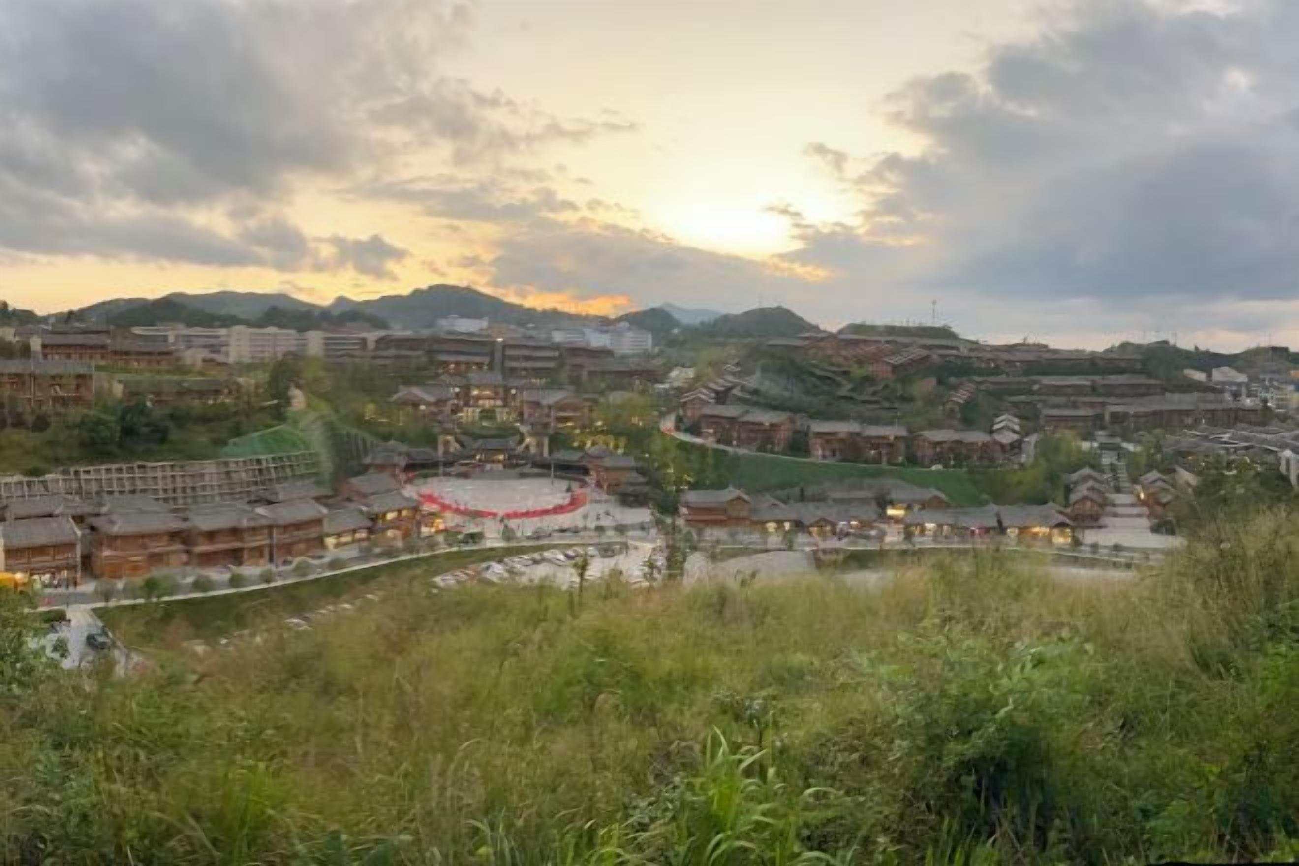 A traditional village with buildings, a river, and a mountainous backdrop.
