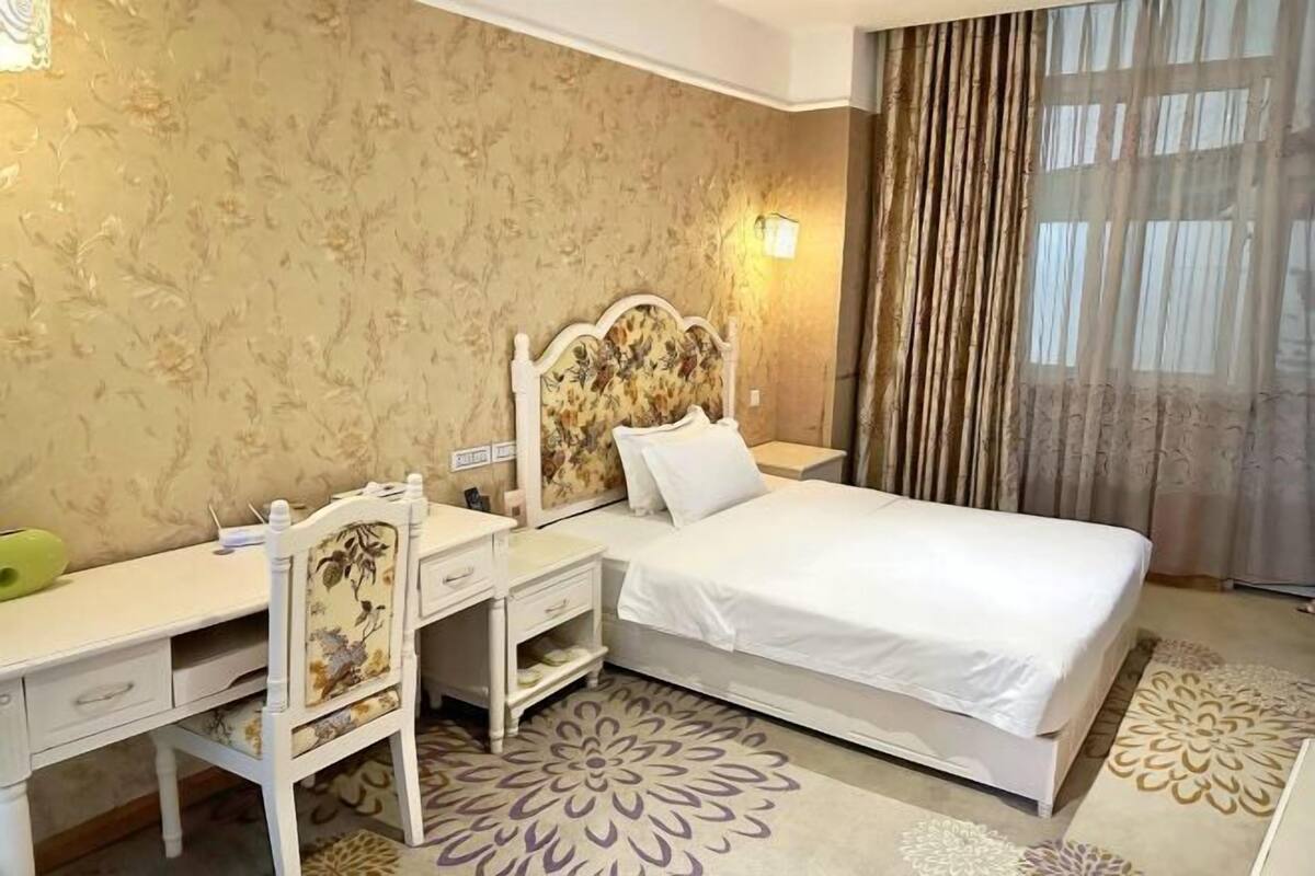 Habitación de hotel con cama, escritorio, silla, mesita de noche y lámpara de pared.