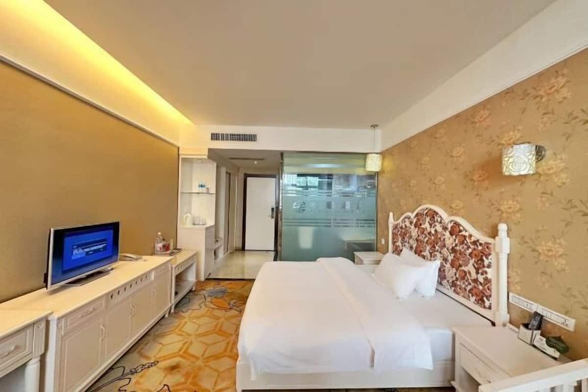 Habitación de hotel con cama, televisor, escritorio y baño visible a través de una puerta abierta.