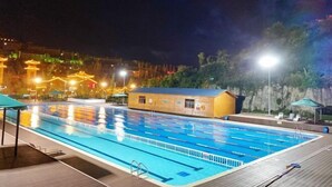Ein Schwimmbecken mit deutlichen Bahnen, umgeben von einer Holzterrasse und einem kleinen Gebäude.