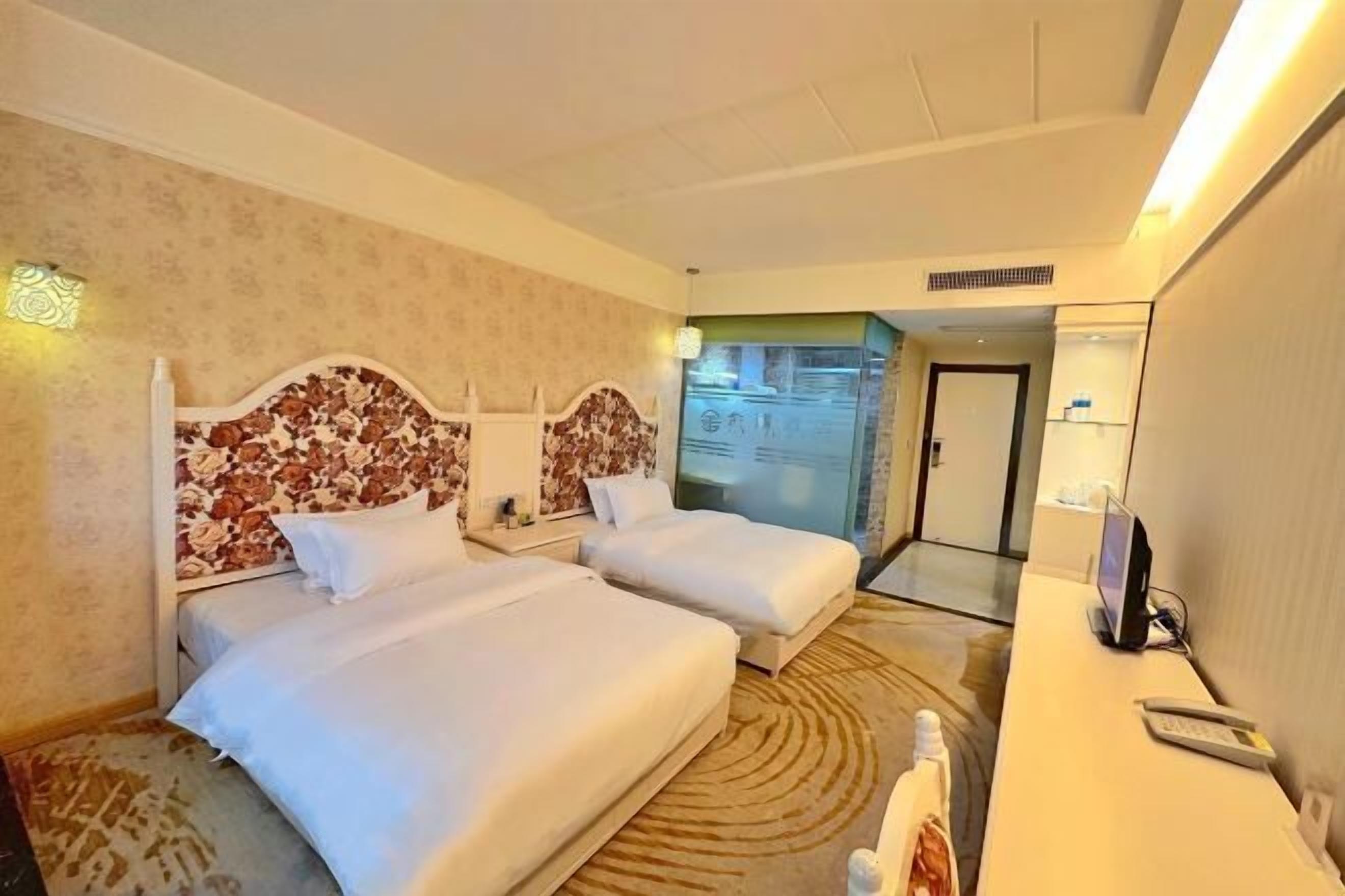 Camera d'albergo con due letti, una scrivania con un computer e un bagno visibile attraverso una porta aperta.