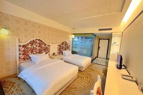 Habitación de hotel con dos camas, un escritorio con computadora y un baño visible a través de una puerta abierta.