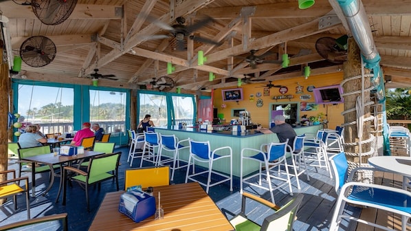 A restaurant with outdoor seating, wooden ceiling beams, and fans.