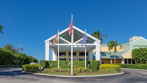 Hotel com entrada coberta, várias bandeiras e paisagismo bem cuidado.