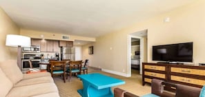 A living room with a sofa, a coffee table, a TV, and a kitchen area with a microwave and refrigerator.