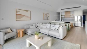 Een moderne woonkamer met een hoekbank, een salontafel en een eethoek, met een keuken op de achtergrond.