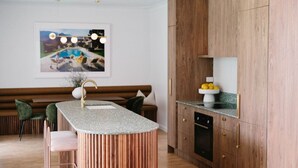 A modern kitchen with a central island, wooden cabinets, and a dining area with a bench and chairs. - Casa Billie ~ Family friendly beachside oasis (Aldinga Beach)