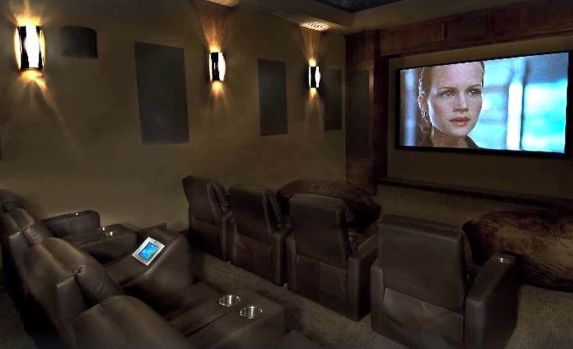 Een thuisbioscoop met leren loungestoelen, een grote flatscreen-tv en wandgemonteerde speakers.