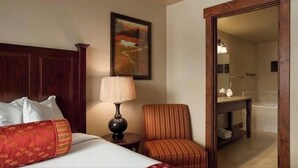 A hotel room with a bed, a chair, a lamp, a painting, and a bathroom visible through an open door. - Grand Lodge Peak 7: True Ski-in Ski-out resort Jan 10-17,2026  Breckenridge, CO  (Breckenridge)