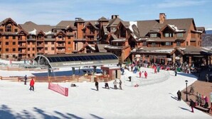 A ski resort with multiple lodge buildings, a ski lift, and a snow-covered slope with skiers. - Grand Lodge Peak 7: True Ski-in Ski-out resort Jan 10-17,2026  Breckenridge, CO  (Breckenridge)