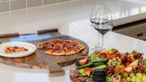 A kitchen counter with a pizza, a wine glass, and a charcuterie board. - The Grape Escape~ Location & style on Shiraz Trail (McLaren Vale)
