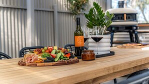A wooden table with a charcuterie board, a bottle of wine, a glass, and a jar of jam. - The Grape Escape~ Location & style on Shiraz Trail (McLaren Vale)