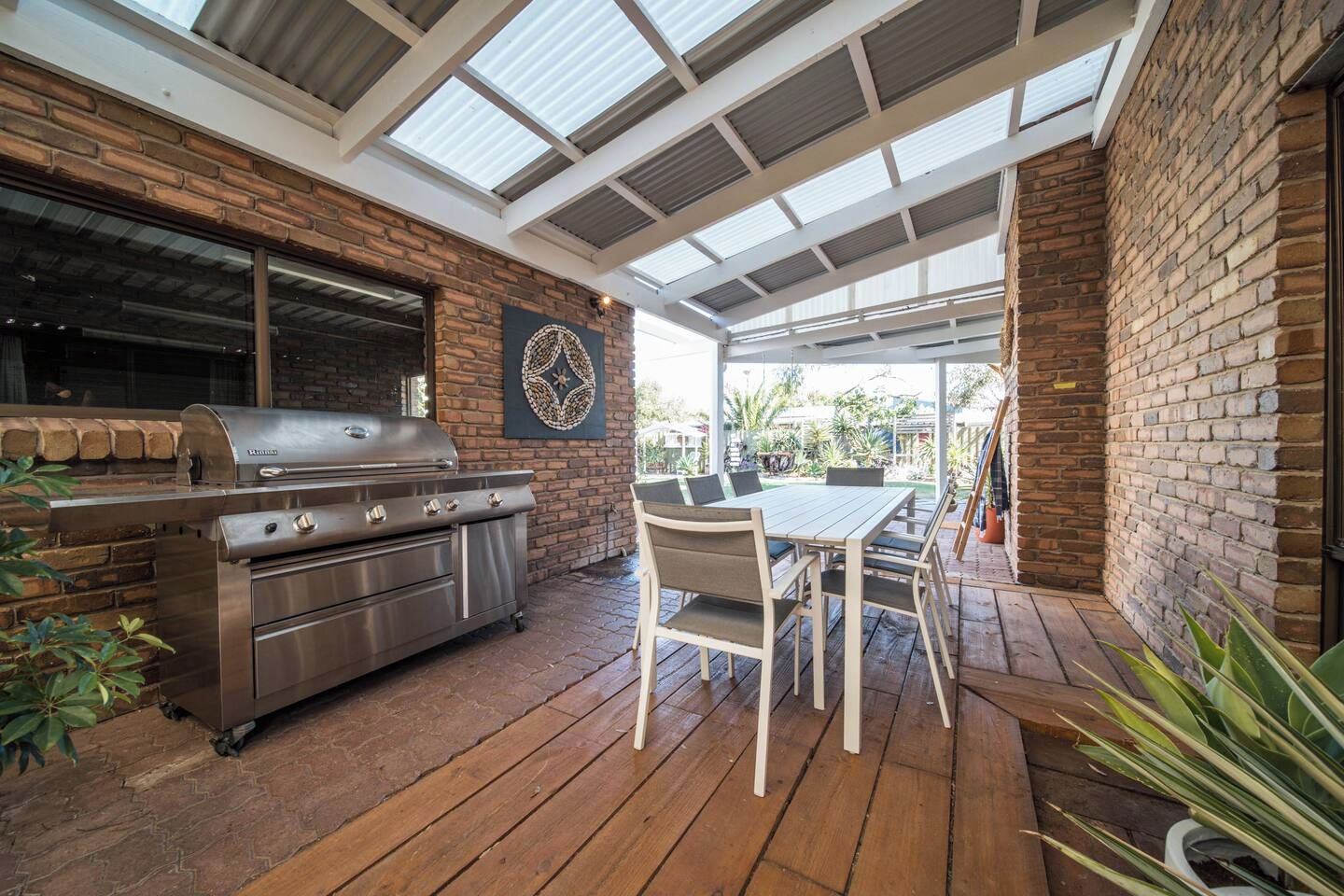 Um pátio externo com churrasqueira, mesa, cadeiras e vista para o jardim.