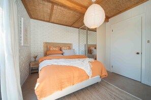 A bedroom with a bed, wooden ceiling, white brick walls, and a door.