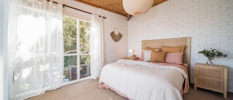 A bedroom with a bed, a nightstand, a wall-mounted lamp, and a window with curtains.