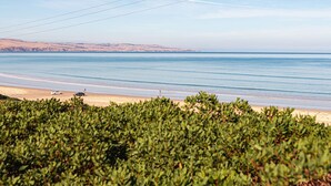 Un paisaje costero con una playa, cielo despejado y colinas al fondo.