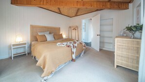 Un dormitorio con cama, mesitas de noche, un armario y techo con vigas de madera.