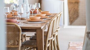 Comedor con mesa de madera dispuesta para seis personas, rodeado de sillas de mimbre.