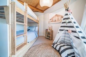 Un dormitorio infantil con literas, una alfombra tejida, una tienda de campaña tipi y un cuadro en la pared.