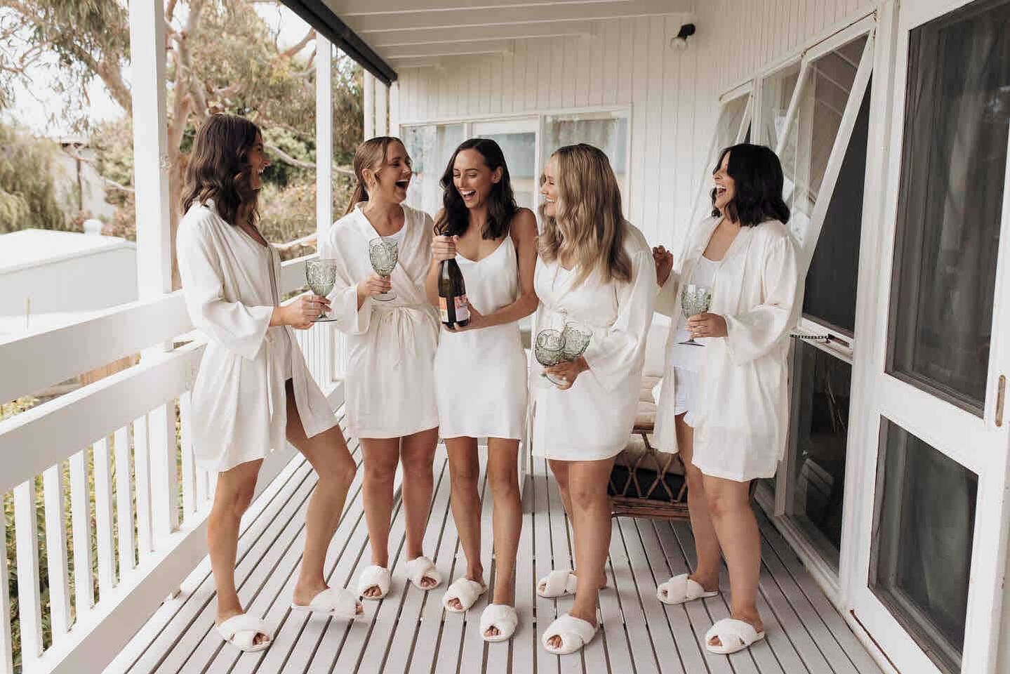 A group of people on a wooden deck with white railings, holding drinks and glasses.