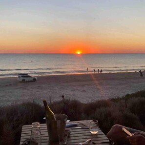 A sunset view from a beachside table with a bottle, glasses, and cutlery. - Salt Bush Beach House~The ultimate Fleurieu escape (Aldinga Beach)