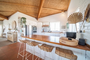 Una cocina moderna con una isla de madera, taburetes de bar y un ventilador grande.