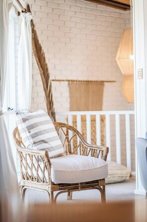 Une chaise en osier, dotée d’un coussin et d’un oreiller à rayures, placée près d’un rideau blanc et d’une fenêtre.
