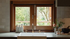 Une cuisine avec une grande fenêtre, un évier et un plan de travail sur lequel se trouvent des bouteilles et une plante.