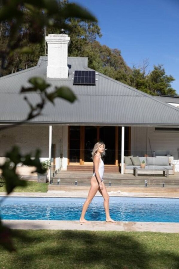 A house with a swimming pool, a covered patio, and a solar panel on the roof.