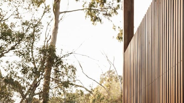Une personne assise dans une baignoire sur une terrasse en bois, avec vue sur les arbres.