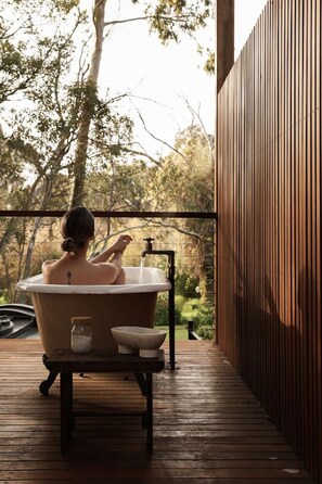 A person sitting in a bathtub on a wooden deck with a view of trees. - Herrings House:  iconic designer nature retreat (Willunga South)