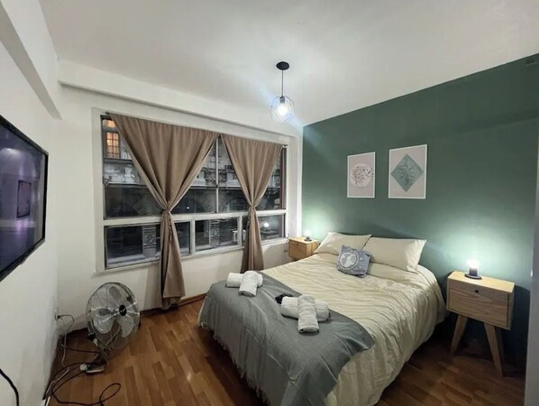 A bedroom with a bed, bedside tables, a fan, and a window with curtains.