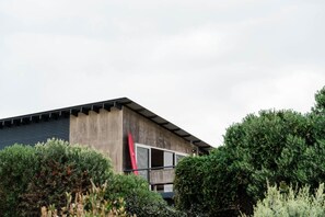 A modern building with a concrete facade, large windows, and a red surfboard leaning against it. - Seaside surf haven, pup friendly - Seafarers Lodge (Middleton)