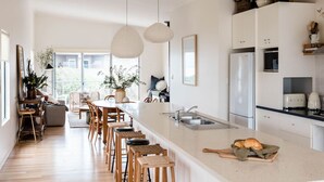 Une cuisine moderne dotée d’un grand îlot central, de chaises en bois, de luminaires suspendus et offrant une vue sur l’extérieur.