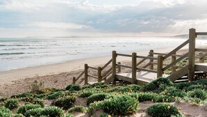Un escalier en bois menant à une plage d’où l’on a une vue sur l’océan.