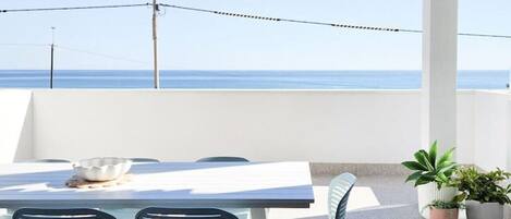 Un patio exterior con mesa y sillas, vista al mar y plantas en macetas.