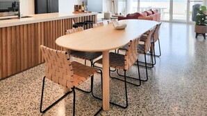 Et moderne køkken med en central ø, et spiseområde med seks stole og et stort vindue med udsigt til det fri.