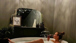 Une personne se détend dans une grande baignoire ronde, dans une pièce aux murs lambrissés et dotée d’un miroir.